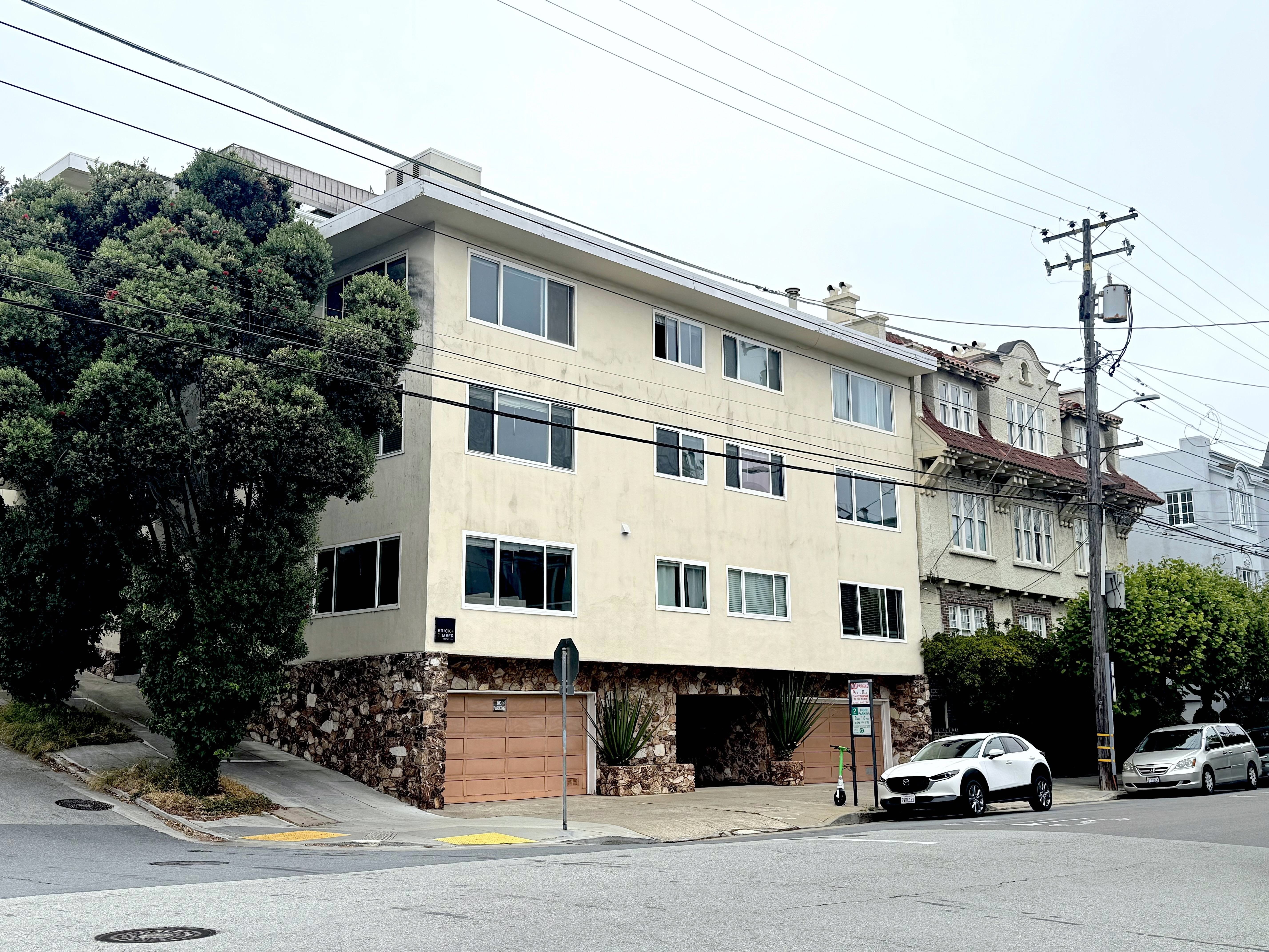 A two-story building with a garage door is situated on a street with cars parked in front.