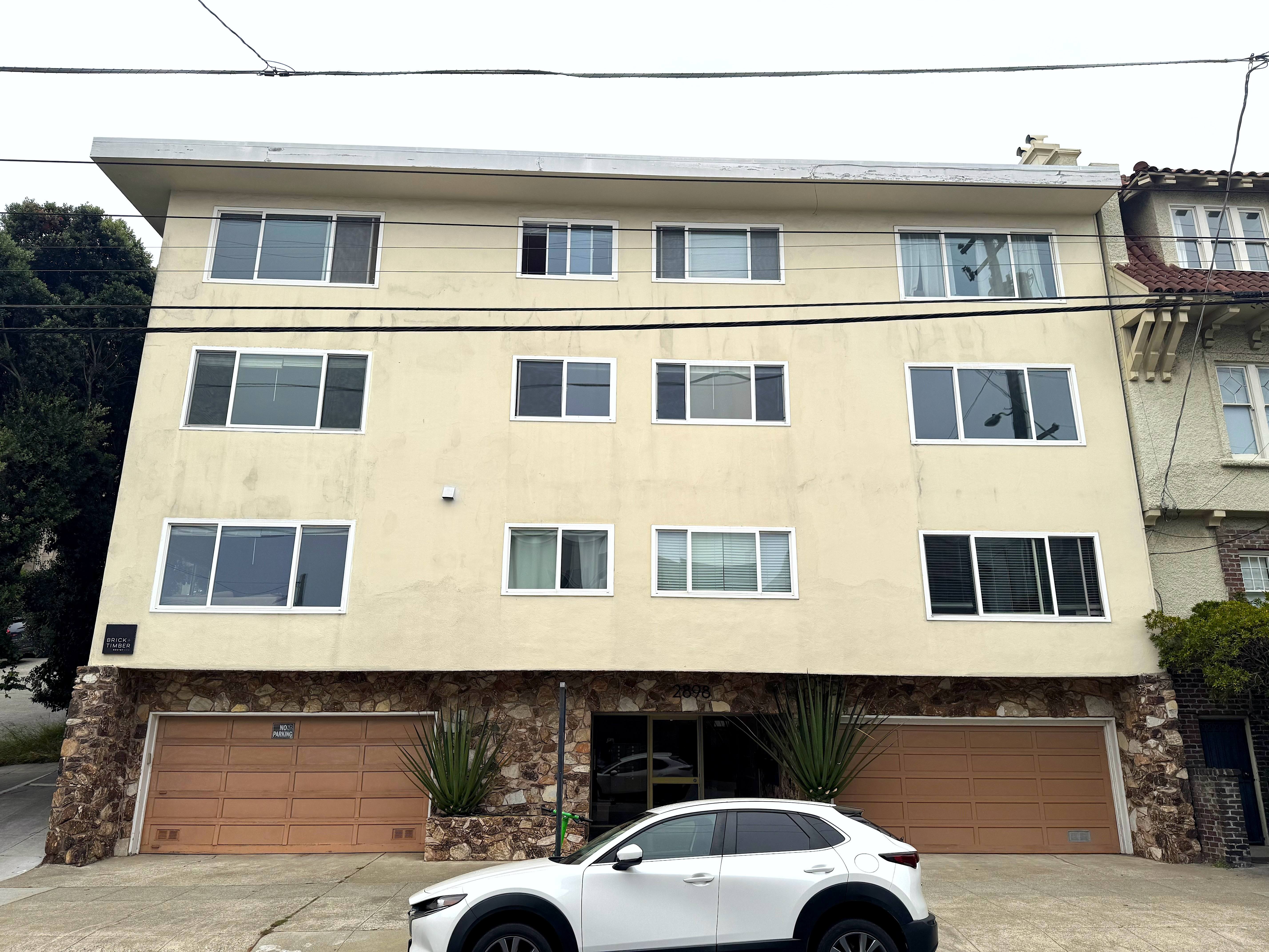 A white car is parked in front of a tan building.