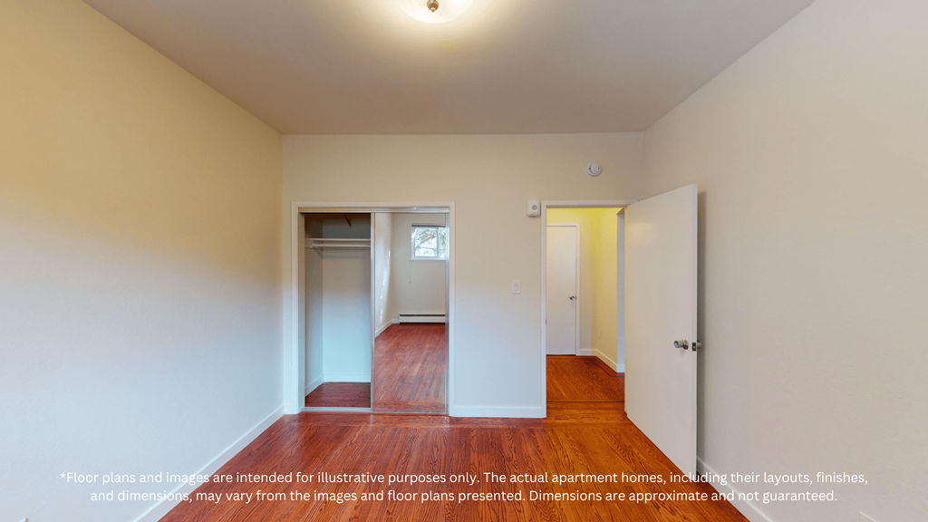 A room with a wooden floor and white walls, with a door on the right and a small window on the left.