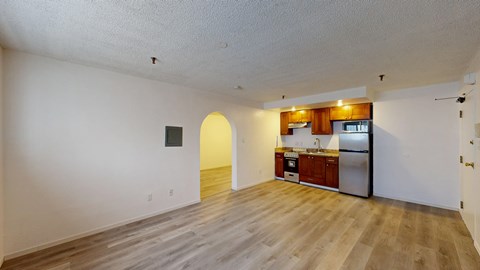 A kitchen with a refrigerator, sink, and cabinets is visible through an archway.