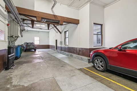A red car is parked in a garage with a concrete floor and white walls.