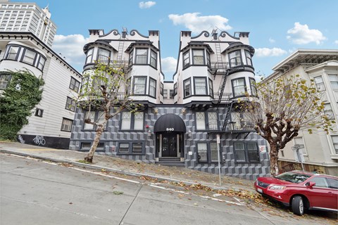 A red car is parked on the sidewalk in front of a building with a black awning.