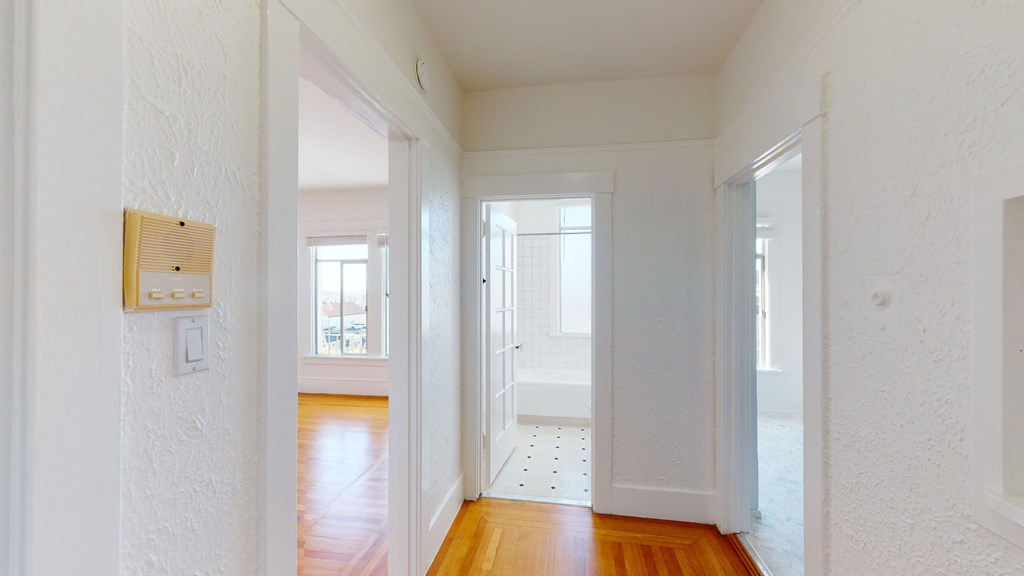 a living room with white walls and wooden floors and a door to a bathroom