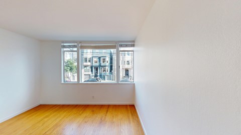A room with wooden floors and a window showing a view of a building.