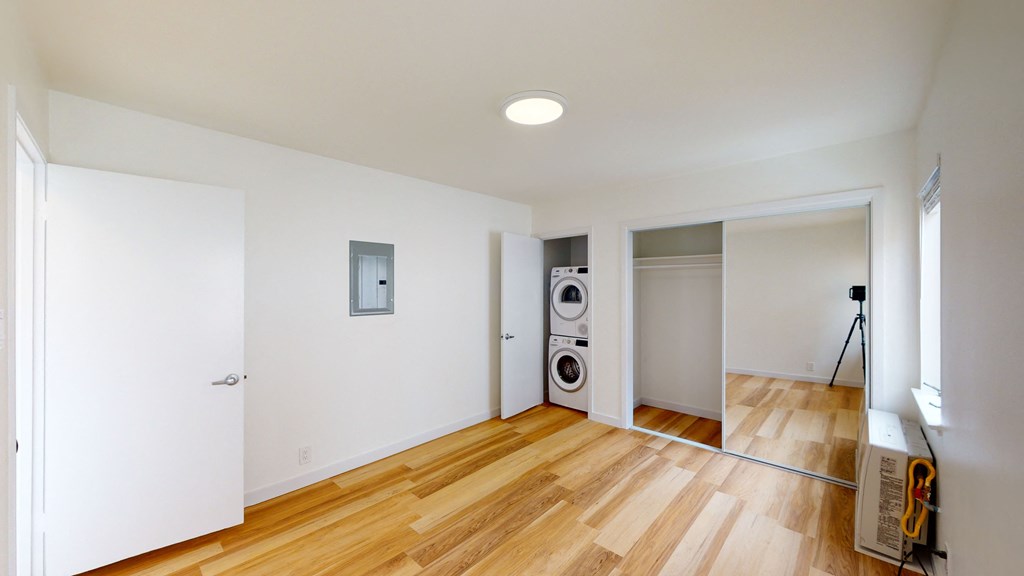 a living room with white walls and wood floors and a washer and dryer
