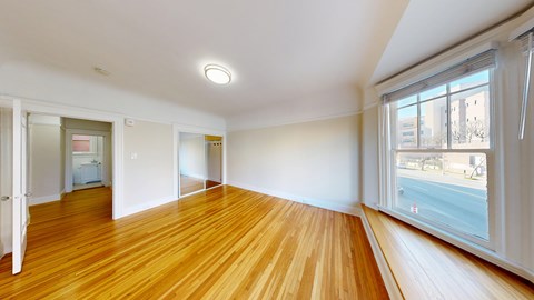 A room with wooden floors and a window overlooking a street.