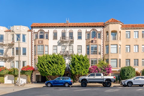 A blue car is parked in front of a building with a red tile roof.