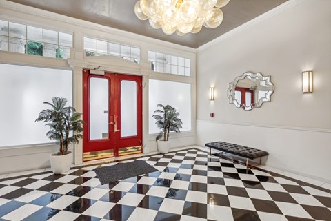 Grand entrance to a building, featuring a double door with a handle, a chandelier hangs from the ceiling, and two plotted plants, one on each side of the door