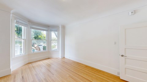 A room with a white door and a window with a view of trees.