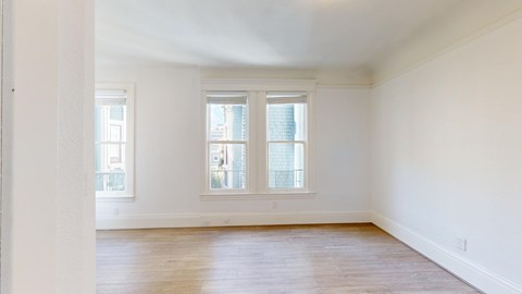 A large empty room with wooden floors and two windows.