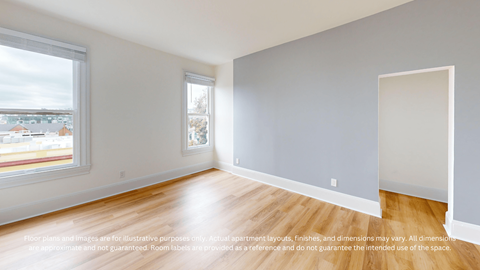 A spacious room with a large window and wooden flooring.