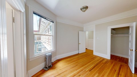 A room with wooden floors and a window overlooking a building.