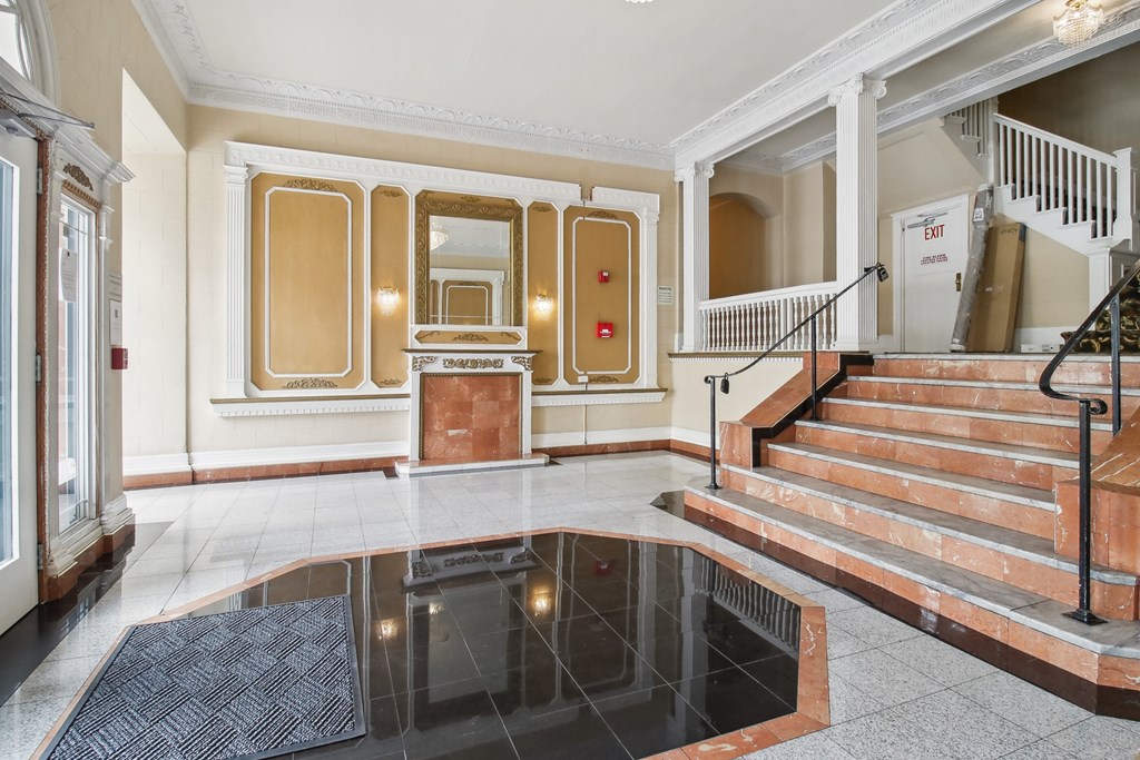 Grand entrance to a building featuring a large mirror above the fireplace and a staircase