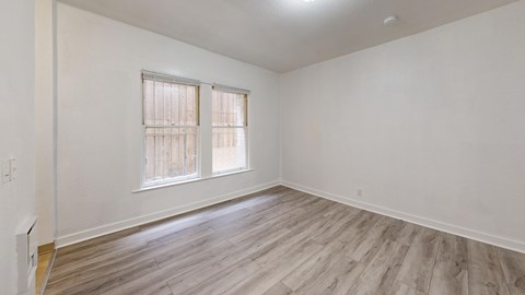 A room with wooden flooring and a window with blinds.