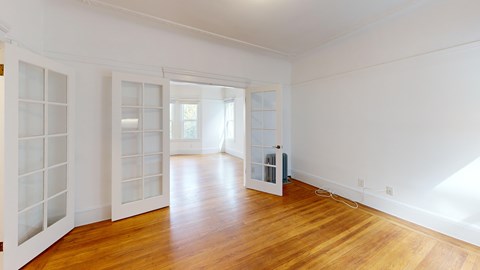A room with white walls and wooden flooring with a white door and a window.