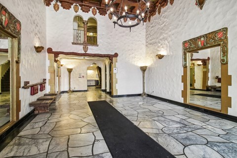 Grand hallway with a high ceiling and a chandelier hanging from the center, a wooden bench and a mirror