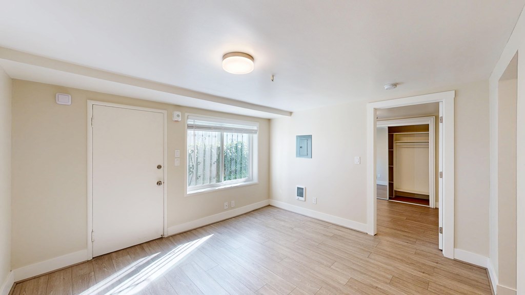 A room with white walls and wooden flooring, with a door on the left and an open door on the right.