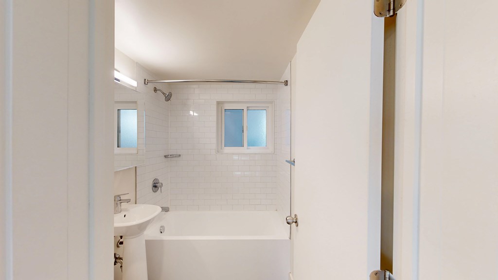 A white bathroom with a tub, sink and mirror.