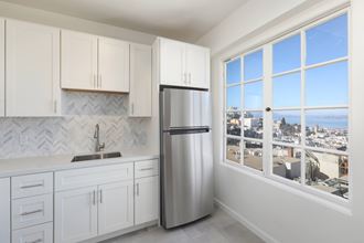 a white kitchen with a large window and a stainless steel refrigerator