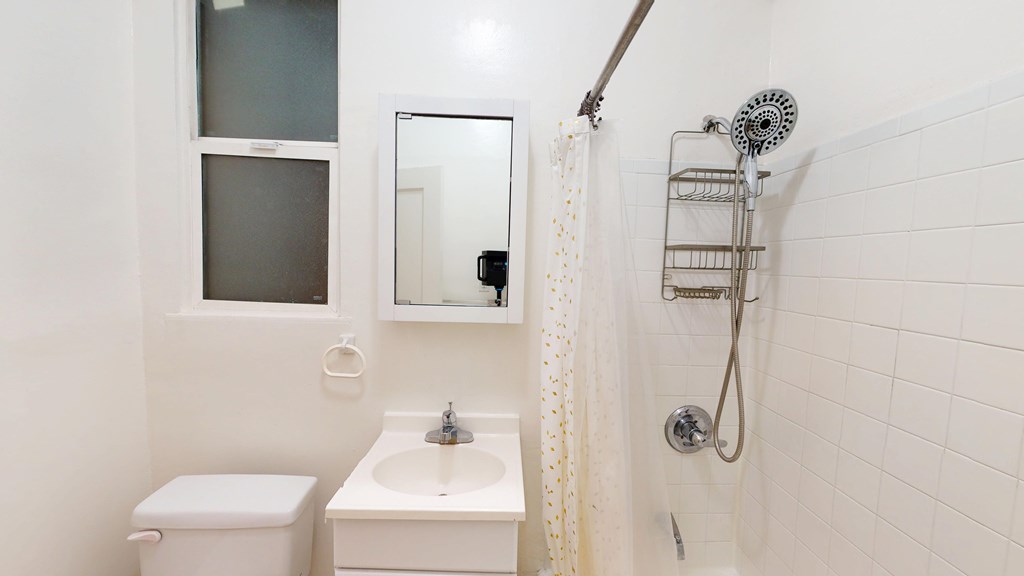 A white bathroom with a toilet, sink, mirror, and shower.