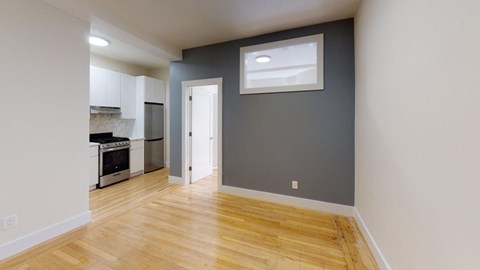 a renovated living room and kitchen with wood floors and a grey wall