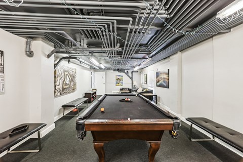 A pool table in a room with a lot of pipes on the ceiling.