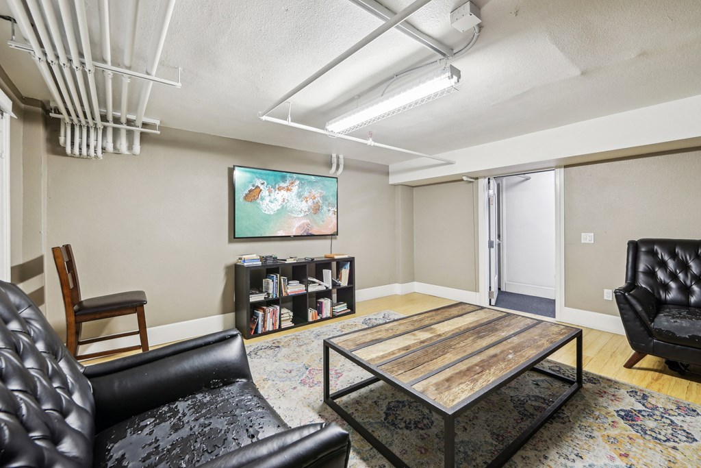Room with a wooden coffee table surrounded with armchairs, bookshelf, and a flat-screen TV