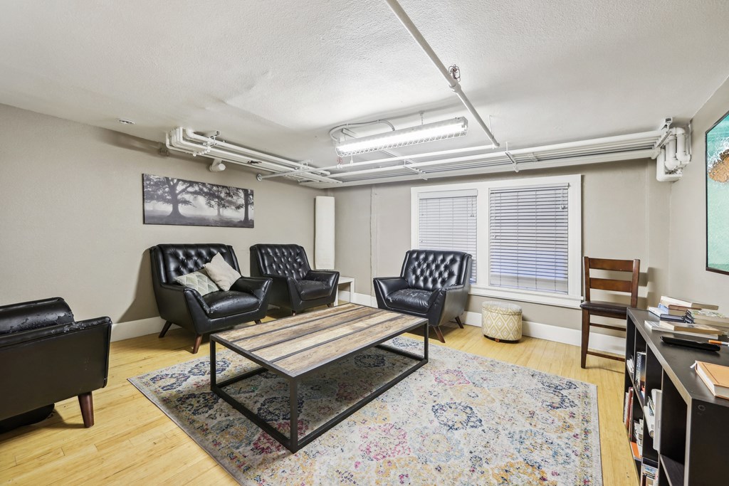 Room with a wooden coffee table surrounded with armchairs, bookshelf, and a flat-screen TV