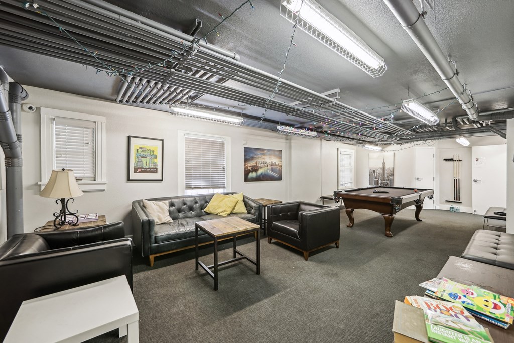 Room with a wooden coffee table surrounded with armchairs, bookshelf, and a flat-screen TV