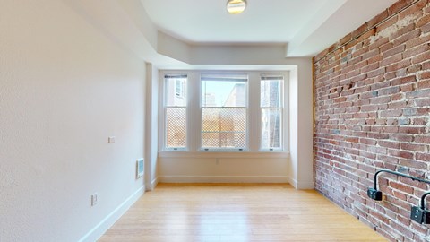 A room with a brick wall and a window with a view of a balcony.