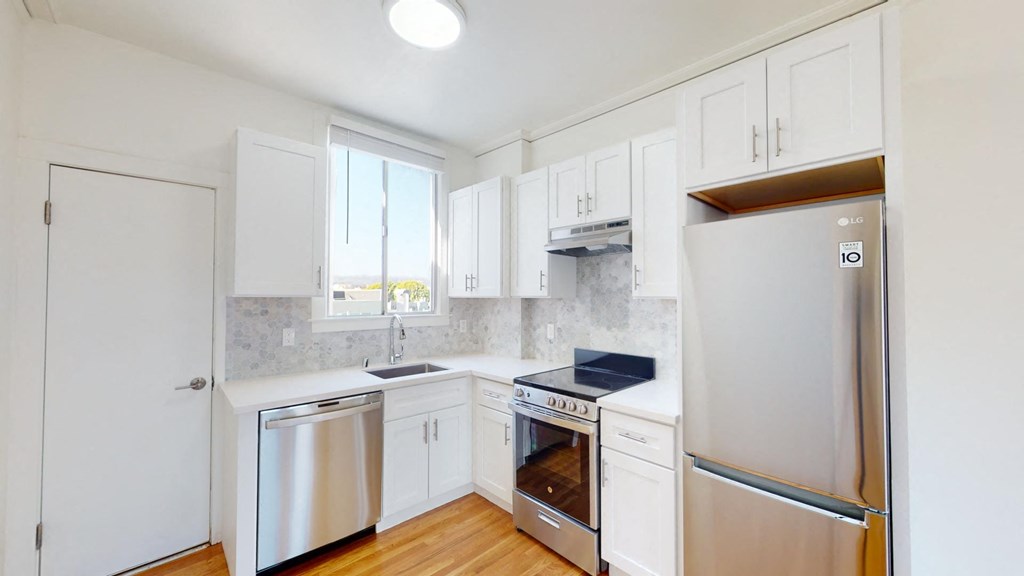 Kitchen with multiple cabinets, refrigerator, stove, range hood, and sink