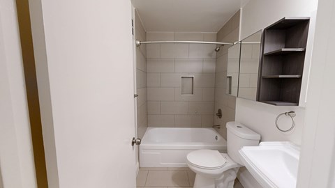 A white toilet is in a small bathroom with a white tub.