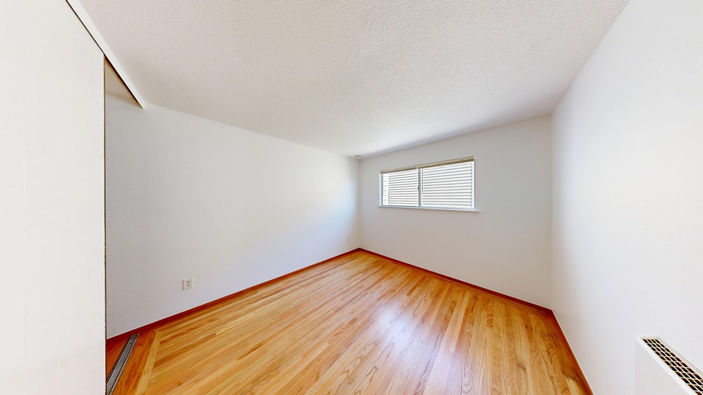 A room with wooden floors and a window with blinds.