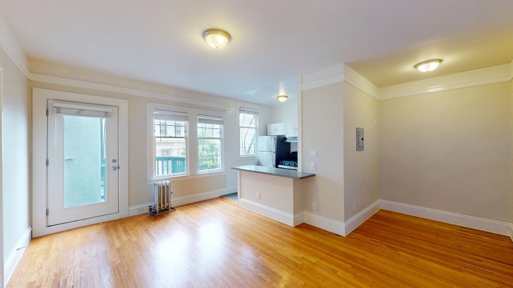 Spacious living room with a wood-like flooring, large windows, and a view of the kitchen