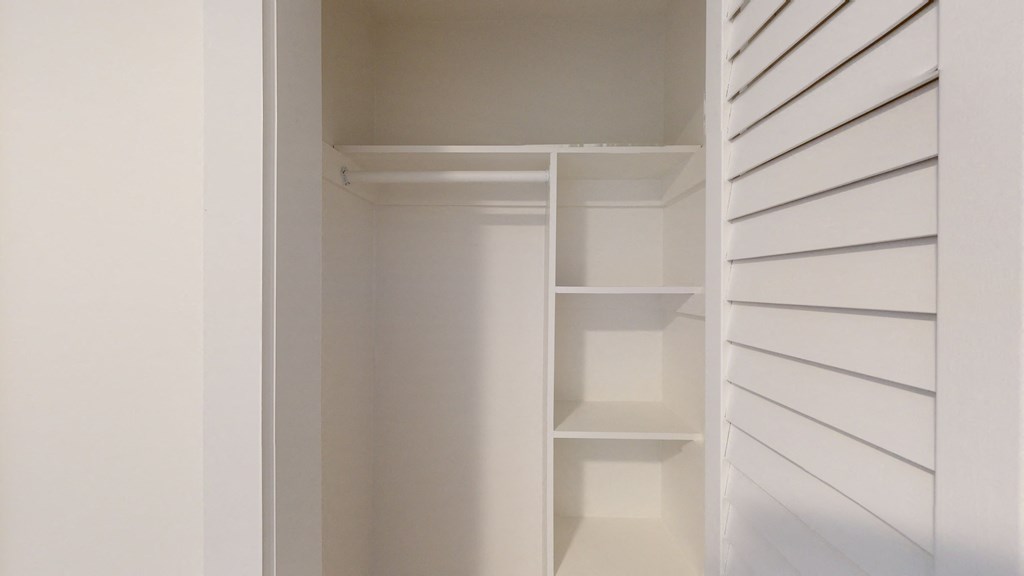 a walk in closet with white shelving and a white closet door