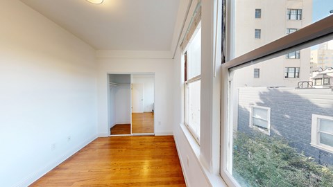 A room with a wooden floor and a large window overlooking a street.