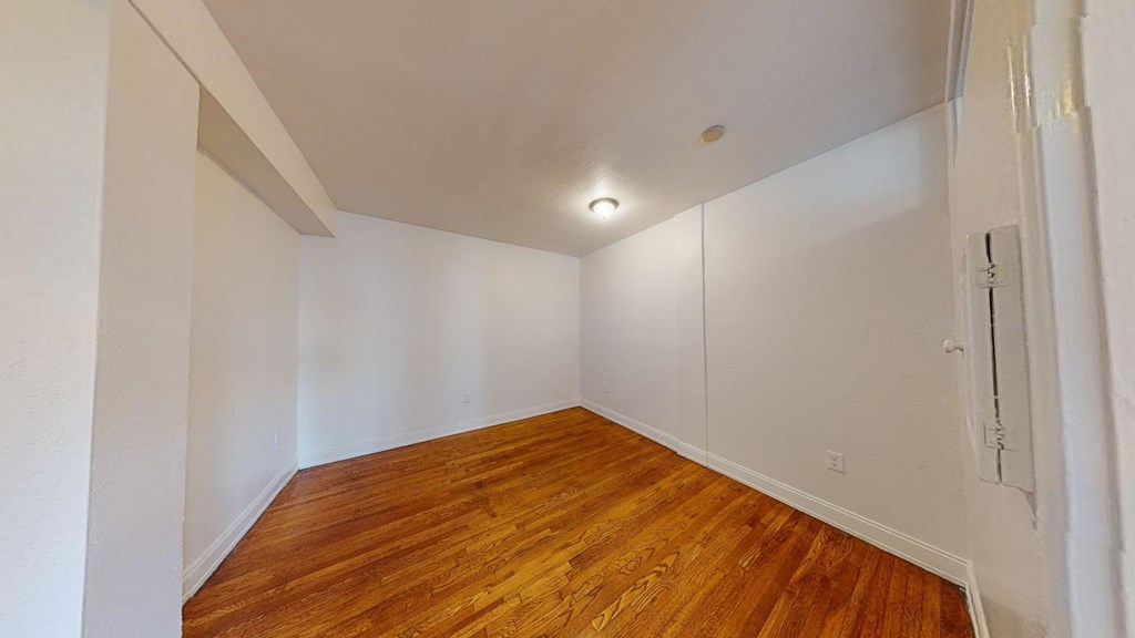 a bedroom with white walls and wood flooring and a closet
