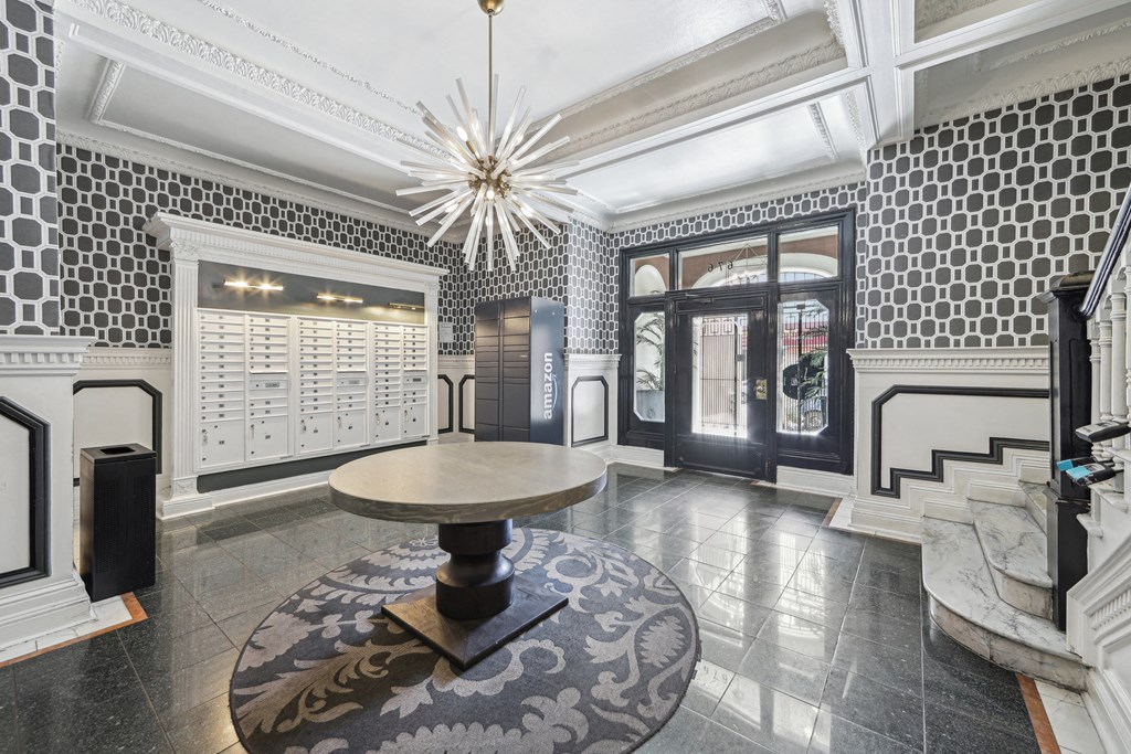 Lobby with geometric wallpaper, mailboxes, an Amazon locker, and a round table beneath a striking chandelier