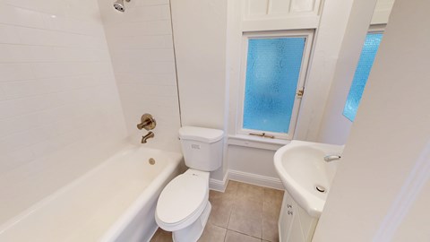 A white toilet is in a bathroom with a white bathtub and a white sink.