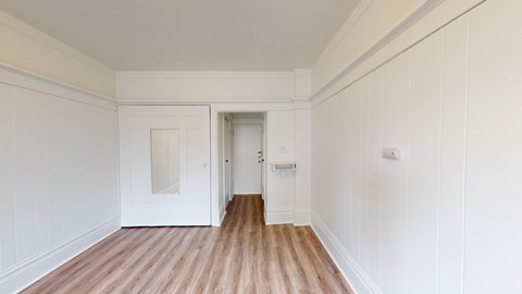 A room with white walls and wooden flooring with a door on the right.