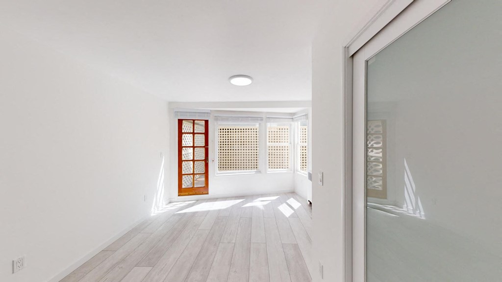 a living room with white walls and a wood floor and a window