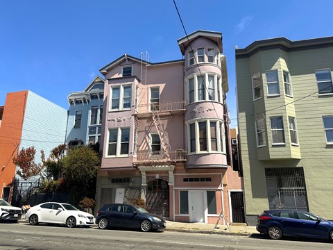 A row of three colorful houses with cars parked in front.