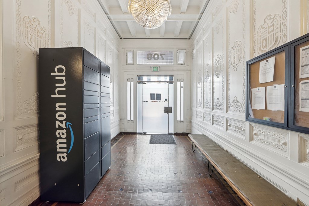 Ornate hallway with Amazon Hub locker, chandelier, bulletin board, wooden bench, and glass door
