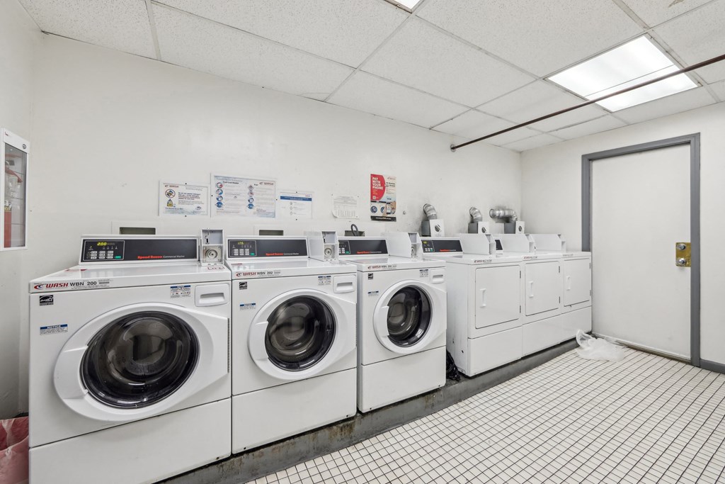 Laundry room with commercial washers and dryers, tiled floor, and posted instructions