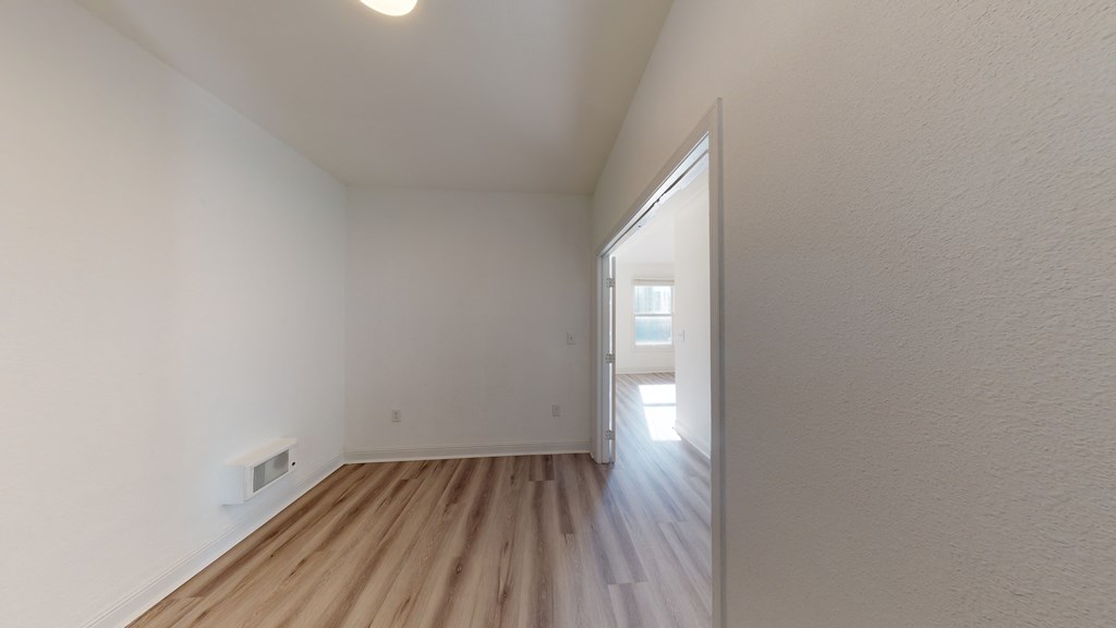 the living room and dining room of an apartment with white walls and wood flooring