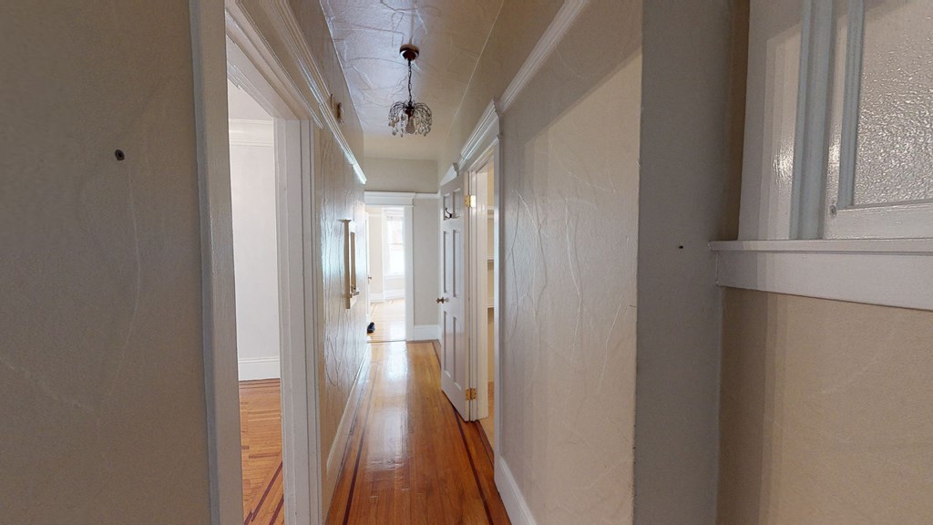 a hallway with white walls and a wooden floor and a chandelier