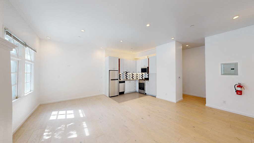 the living room and kitchen of a house with white walls and wood floors