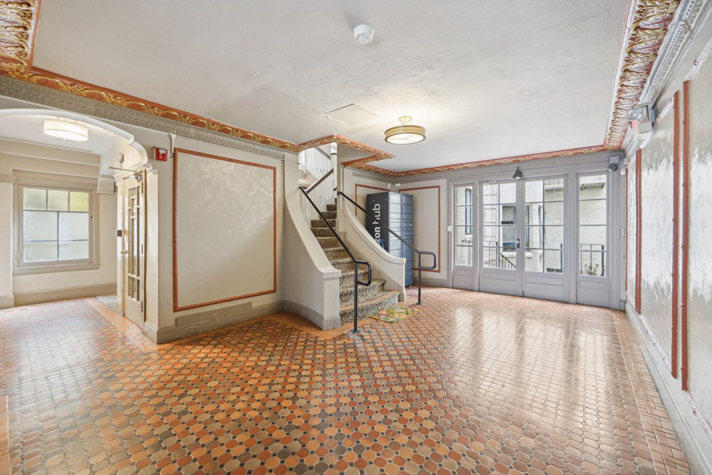 Hallway is illuminated by a chandelier hanging from the ceiling, and a window on the far left side allows natural light to enter the room