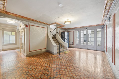 Hallway is illuminated by a chandelier hanging from the ceiling, and a window on the far left side allows natural light to enter the room