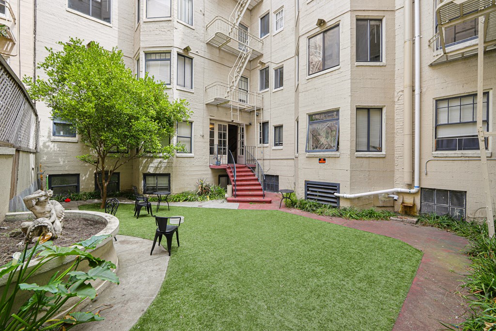 Courtyard with a fence, covered in lush green grass, and a brick walkway leads up to the entrance of the building